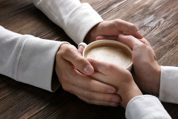 Poster - Lovely couple holding cup of coffee in hands on wooden background