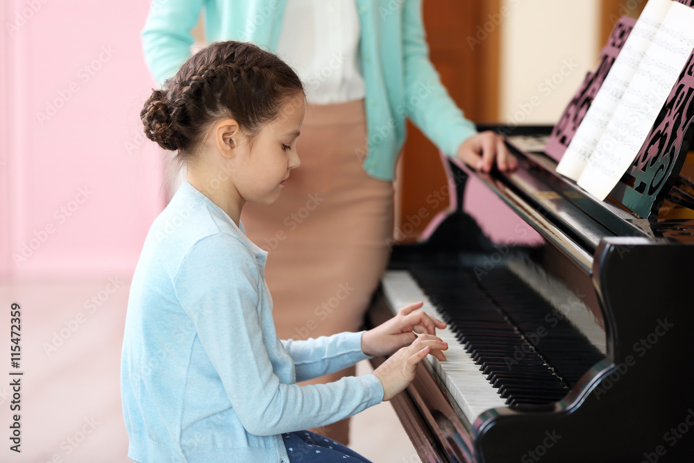 Small girl learning play piano with teacher