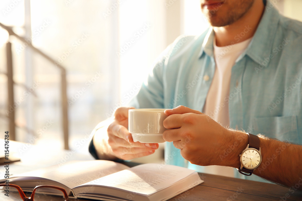 Young man reading book and drinking coffee at the table