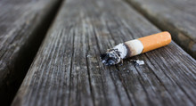 Selective Focus On Cigarette Butt With Ash Isolated On Wood Back