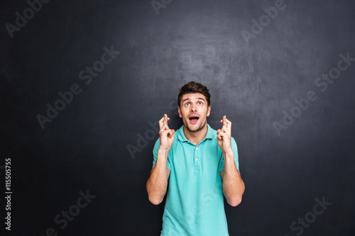 Photographie Handsome young man with his fingers crossed isolated over black