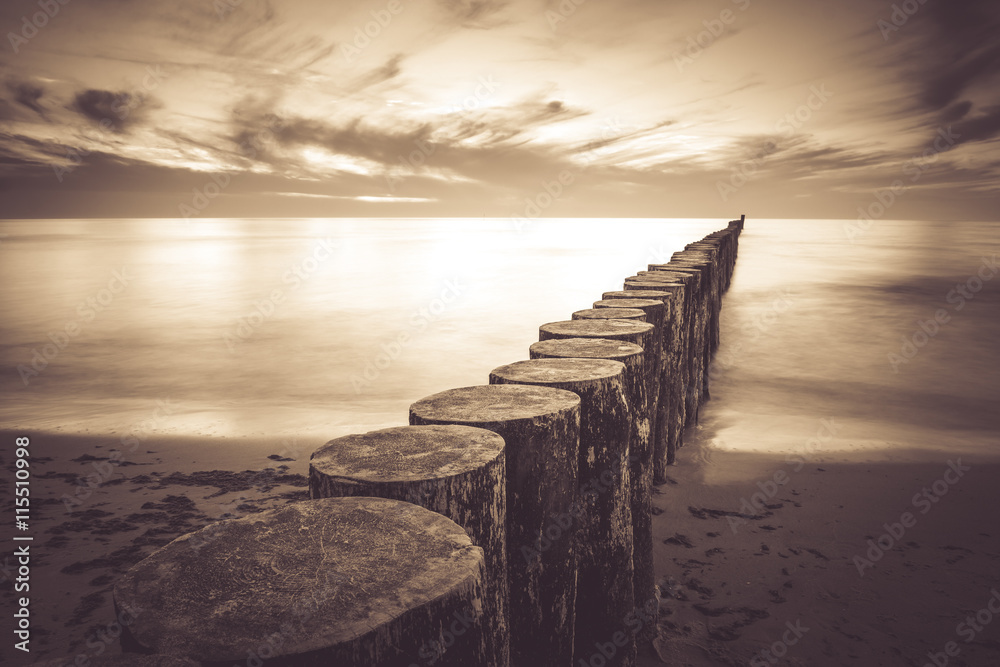 Coast with piles during sunset, long exposure blurring water.Vintage photo of baltic, Poland. - obrazy, fototapety, plakaty 