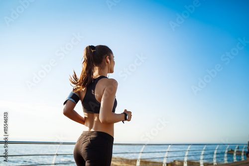 Foto Picture of young attractive fitness girl jogging with sea on background