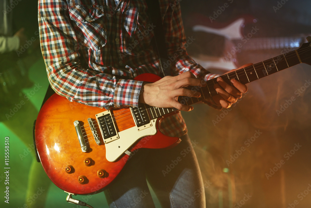 Young man playing electric guitar on lighted foggy background