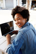 © mimagephotos - Cool young african woman working on laptop at outdoor cafe