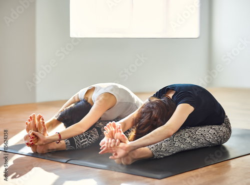 Poster Two young women doing yoga asana seated forward bend