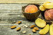 Sliced and whole juicy peaches in coconut shell on wooden background