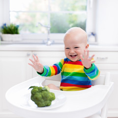 Wall Mural - Little boy eating broccoli in white kitchen