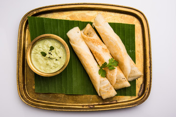 3 dosa rolls with coconut chutney in a brass tray over coconut leaf, favourite south indian meal