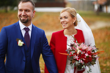 Handsome groom with earings smiles while walking with a blonde b