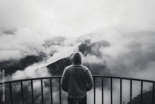 View from behind of a man standing at view point looking to beautiful landscape with foggy mountains in the distance Poster