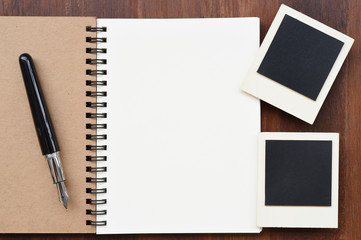 Blank notebook with pen and photo frames on wooden background.