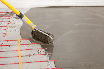 Electric floor heating system installation in new house. Worker align cement with roller