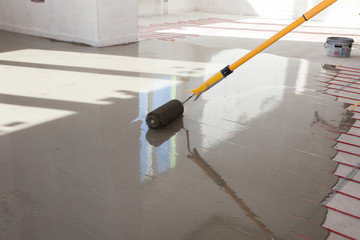 Electric floor heating system installation in new house. Worker align cement with roller