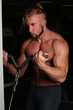 © kazanovskyiphoto - Handsome muscular man holding simulator on dark  background