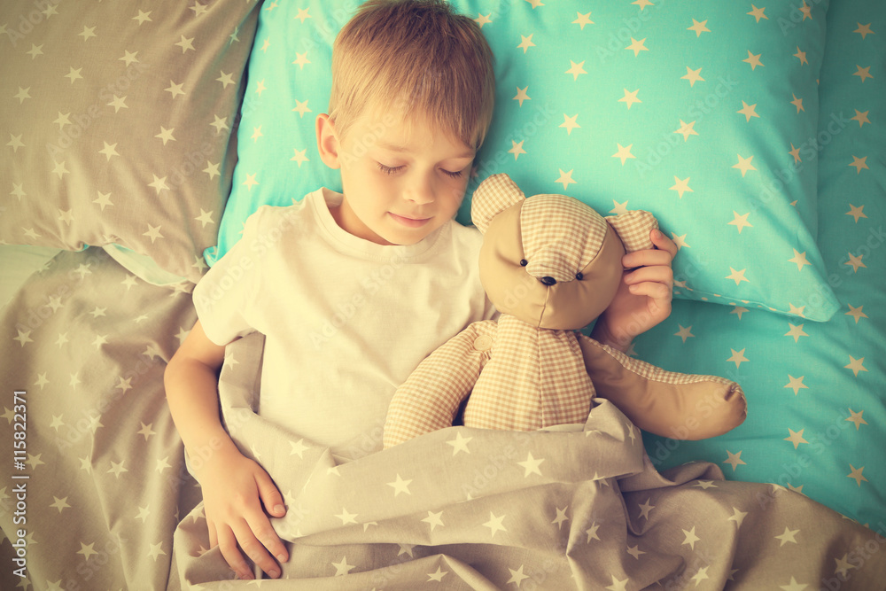 Adorable little boy sleeping with teddy bear in bed