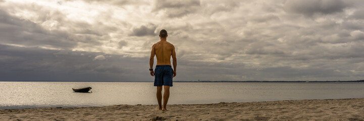 Sporty man walking at the beach, boat on the ocean