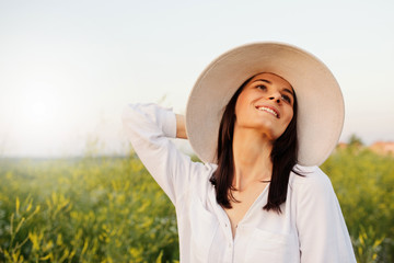 Canvas Print - Portrait of a romantic beautiful and attractive young woman with a hat and white shirt, dreaming, looking up on the sky, on nature, field background. Beauty