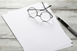 White page with pen and eyeglasses on table