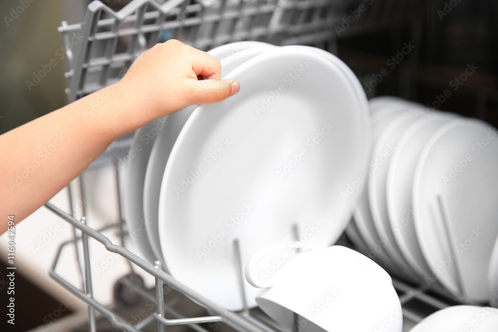 Little girl taking plates from the dishwasher, closeup