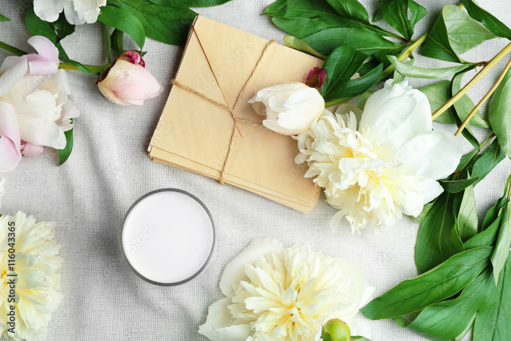 Composition with beautiful peony flowers and envelopes on white fabric, top view