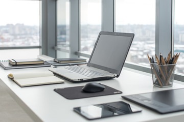 workplace with notebook laptop comfortable work table in office windows and city view.