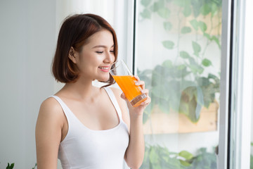 Wall Mural - Pretty young asian woman in bright room drinking orange juice