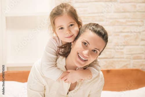 Fotografia Beautiful little girl embracing her mother while sitting on the bed at home
