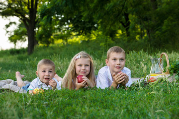 girl and two boys lay on stomach on the green grass and eat apples