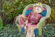 Scarecrow Sitting In A Wicker Chair In Garden