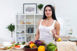 © undrey - Young woman standing next to kitchen table with fresh vegetables drinking milk in the morning.
