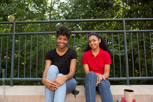 Fotografie, Obraz 2 young african american college students sitting on a sidewalk on campus
