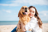 Tender smiling young woman hugging her dog on the beach