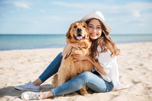 Cheerful Young Woman Sitting And Hugging Her Dog On Beach