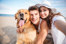 Happy Couple Hugging Their Dog And Smiling On The Beach