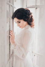 Fantasy Woman Sad Lady In White Vintage Dress Standing In A Large Castle Room White Window, Fantastic Fairy Tale Princess, Trendy Historical Gown. Elegant Girl Medieval Outfit Silk Clothes 