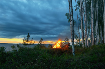 Wall Mural - Big night bonfire by the river at sunset .