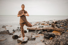 Woman Doing Yoga Tree Pose Namaste On The Stone Near The Ocean