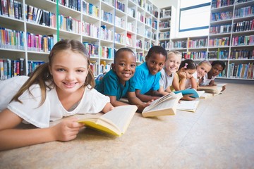 Poster - Smiling school kids lying on floor reading book in library 