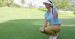 © Dash - Woman wearing white visor and blue polo shirt squats on golf course while holding club and ball