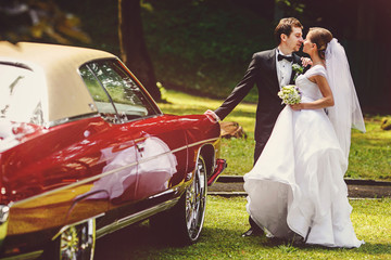 Newlyweds kiss behind an old American car