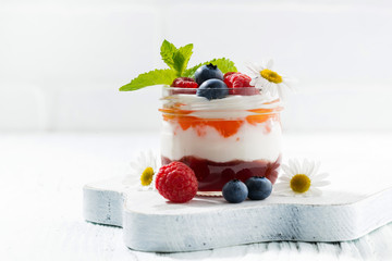 dessert with jam, cream and fresh fruit in a glass jar on white