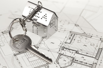 key with keychain in the form of a silver-colored house on a background of architectural drawing