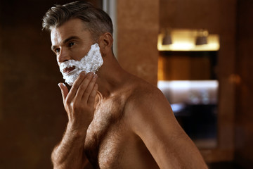 Man Using Shaving Cream On Face In Bathroom. Men Skin Care