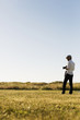 © Astrakan Images - Man with camera standing in grassy field on sunny day