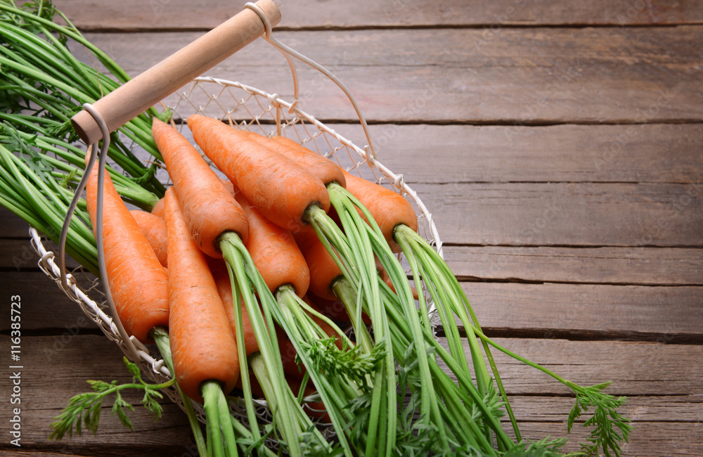 Fresh carrots in basket on wooden table