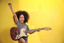 Afro-American Little Girl With Curly Hair Playing Guitar On Yellow Background