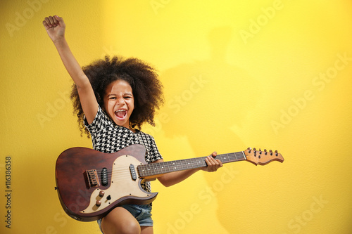 Afro-American little girl with curly hair playing guitar on yellow background Fototapet