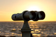 White telescope stands on sea coast in front of golden sunset