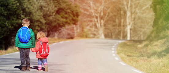 brother and sister with backpacks walking on the road